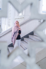 Close up portrait of happy young Asian woman wearing hijab, Islamic stylish modern fashion, smiling and posing on stairs with pattern frame at Shah Alam Mosque.