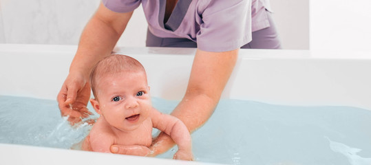 Swimming instructor teaches infant baby to swim. Aquatic therapy for infant baby