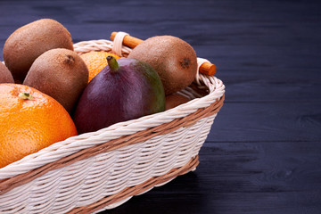 Fresh tropical fruits in basket. Stack of colorful fresh fruits in a basket on dark wooden surface...