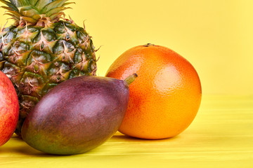 Fresh ripe fruits on yellow background. Flat lay fresh tropical fruits including mango, pineapple, grapefruit and pomegranate.