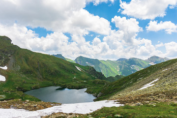 Fototapeta premium summer time in romanian carpathians. beautiful landscape of fagaras mountains. lake capra down in the valley. fluffy clouds above the ridge. view from the slope of Saua Caprei