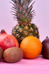 Fresh tropical fruits on pink wood. Set of fresh exotic fruits including pineapple, pomegranate, orange, kiwi fruit and mango on color background.