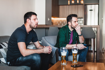 Two guys drinking beer watching sports on TV