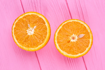 Ripe orange cutted on two halves. Two halves of juicy oranges on pink wooden background.
