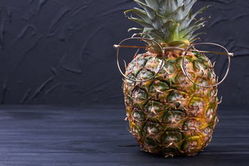 Pineapple with eyeglasses and copy space. Hawaiian ananas wearing glasses on dark background.