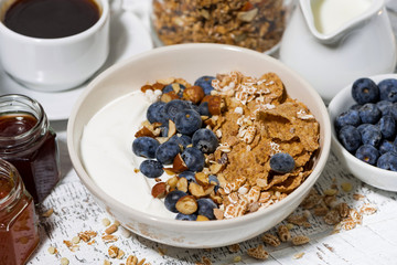 bowl of healthy wholegrain flakes, yogurt and fresh blueberries on white table, closeup