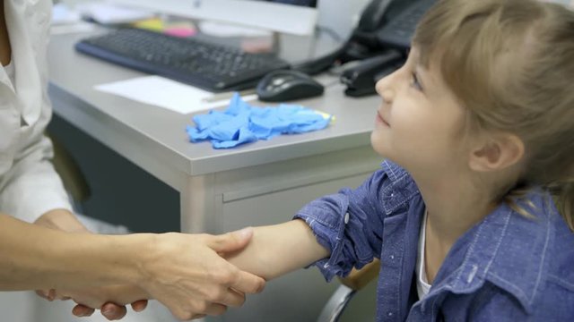 Female pediatrician doctor in white coat palpating arm of cute little girl during medical checkup