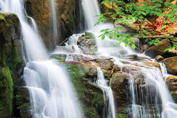 waterfall with small cascades. beautiful nature background in summer. branch with green leaves above. long exposure