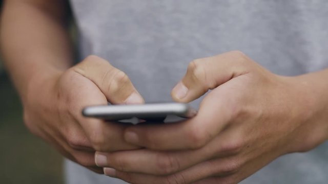Front angle close up shot of a young male scrolling and typing on his phone outside