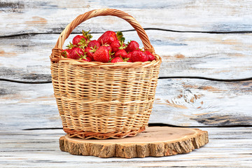 Fototapeta na wymiar Ripe juicy strawberries in wicker basket. Basket of sweet organic berries on natural slice of tree. Beautiful summer composition.