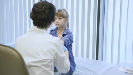 Little girl visiting doctor for medical checkup: female pediatrician in white coat and gloves rolling up her sleeves and palpating her arm