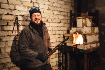bearded man blacksmith gets a red-hot billet out of the furnace.