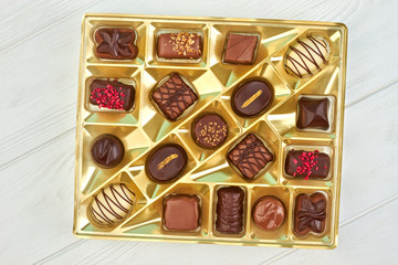 Chocolate candies in box, top view. Assorted candies in golden box on white wooden background.