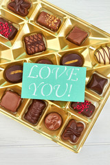 Valentines Day background with chocolate candies. Assortment of candies in box and card with text love you, top view. Happy Valentines Day.