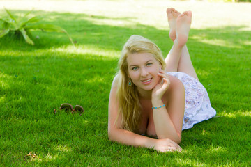 Young blonde beautiful woman laying at grass lawn in summer sexy dress.