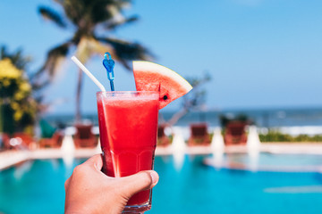 Healthy concept, Hand holding water melon smoothie with swimming pool and blue sky background.