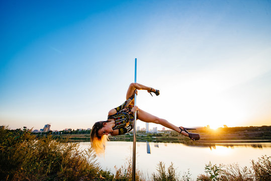 Contrast silhouette photos at sunset against the sky: girl poledancer performs an element on the pole with the split