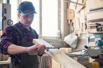 The worker makes measurements of a wooden board with corner ruler.