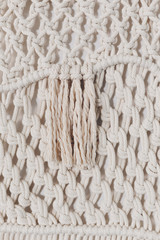 Detail of cream macrame decor displayed hanging on a wall.