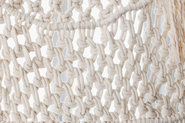 Detail of cream macrame decor displayed hanging on a wall.