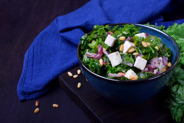 Salad with kale, red onion, feta cheese and pine nuts in the blue bowl