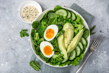 healthy green salad with avocado, eeg, broccoli, cucumber, green peas and spinach in white  bowl