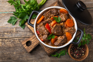 beef stew with vegetables in black pot on dark wooden background,