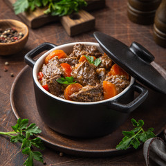 beef stew with vegetables in black pot on dark wooden background,