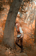 forest robber rests leaning against a tree in the autumn orange forest. a lovely girl with bright...