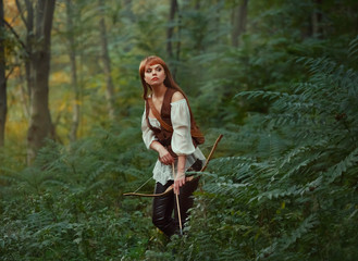gorgeous lady with long red hair in leather clothes follows wild animal, hunts down prey in rainforest, rite of initiation into hunters, girl pulled bowstring of bow with arrow, ready to shoot
