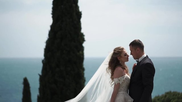 Young beautiful bride in a wedding dress and groom hugging and kissing outdoors. Newlyweds near sea.