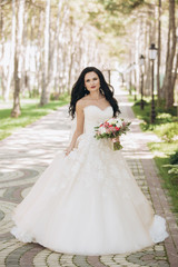 Fototapeta na wymiar Beautiful bride in a white wedding dress on outdoors. Holding a wedding bouquet