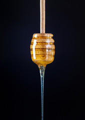  A drop of honey flows down from a honey dipper on a black background. A drop of honey flows down from a honey dipper on a black background.