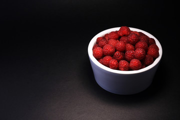 Ripe raspberry. Raspberry in a white ceramic bowl on black background.