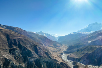 Fototapeta premium Trek in Annapurna Circuit, Himalayas, Nepal. Trail goes on from Manang along the river, those who lock back are rewarded with beautiful view on the river, reflecting rays of the rising sun. Sunrise