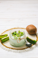 Yogurt with kiwi slices on a wooden white background.