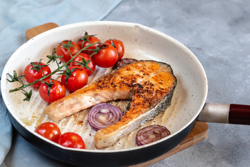 Fried salmon in a frying pan with tomatoes and red onion.