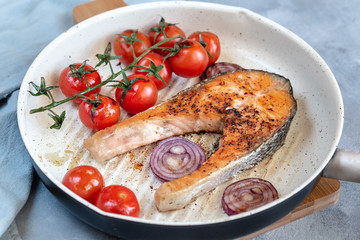 Fried salmon in a frying pan with tomatoes and red onion.