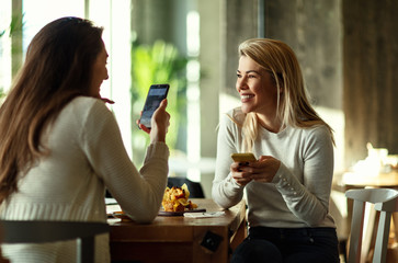 Happy women using mobile phone and talking while relaxing in a cafe.