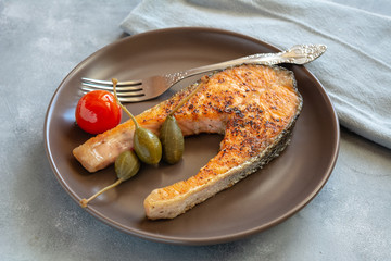 Fried salmon served on plate with caper apples and tomato.