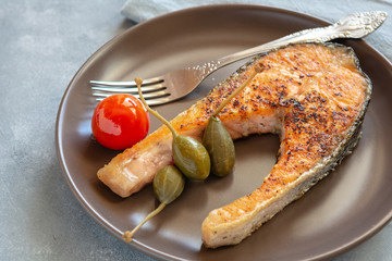 Fried salmon served on plate with caper apples and tomato.