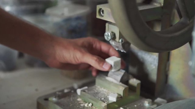 Hands of anonymous artisan using manual cutter to divide tiny cube on two parts while making mosaic in studio