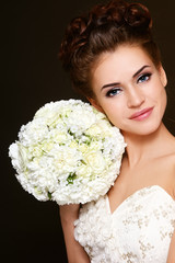 Young beautiful happy bride with winged eye make-up and prom hairdo holding fancy bouquet in her hand