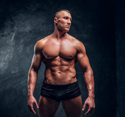 A handsome athletic man with perfect pumped body wearing underwear. Studio photo with dark wall...