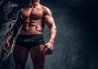 Fototapeta na wymiar Athletic man with muscular body wearing underwear. Cropped photo in a studio with dark wall background 