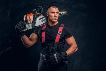 Young brutal logger posing with a chainsaw on his shoulder and looks sideways