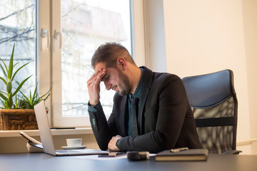 Naklejka premium businessman working on laptop in office headache by window black table with notebook papers phone migraine