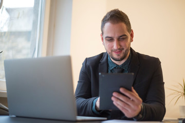 businessman working on laptop in office taking notes on tablet