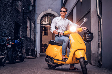 Fototapeta na wymiar Fashionable man wearing sunglasses riding on vintage Italian scooter in the old narrow street of Europe