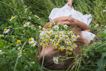 Beautiful little girl in a white dress is lying on a green meadow with a bouquet of daisies